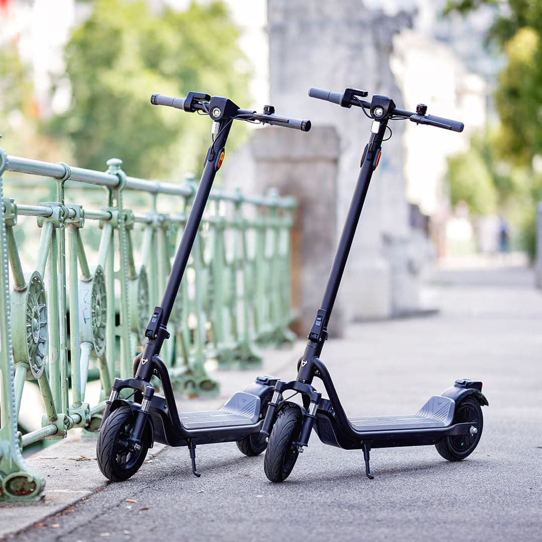 Two NIU KQi 100 Series electric scooters parked beside a city railing
