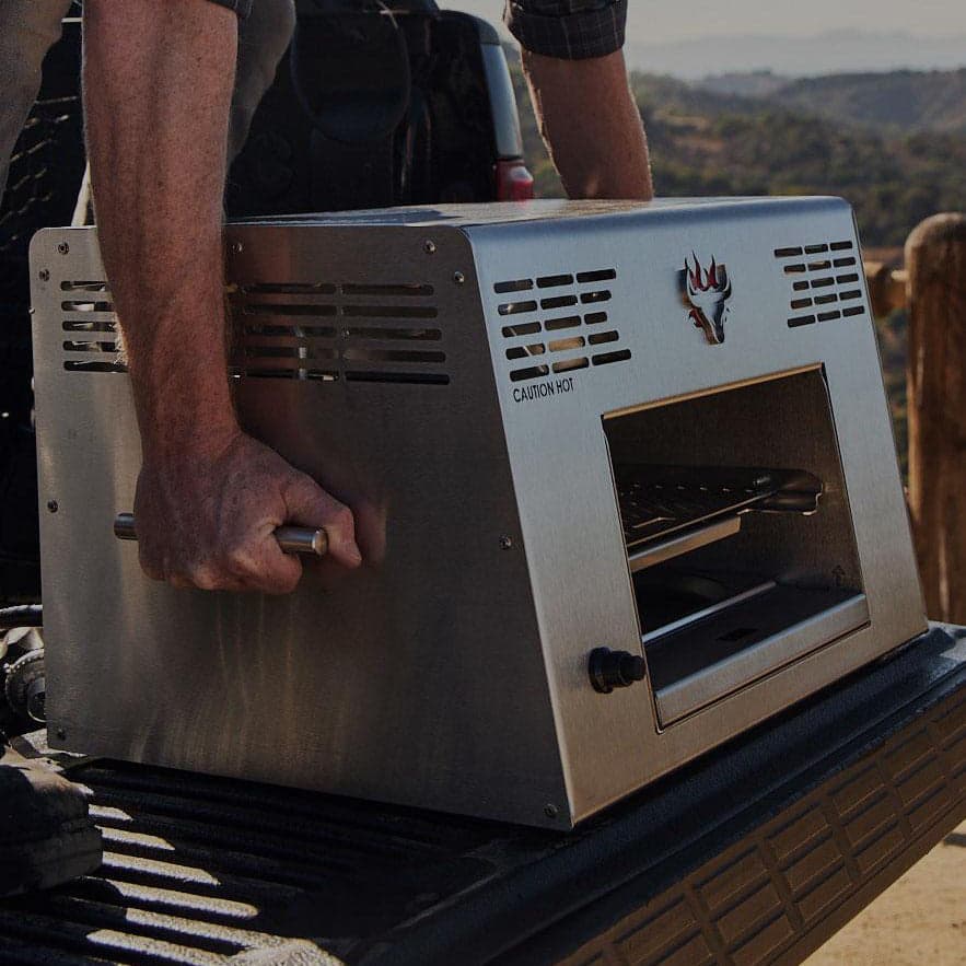 A person lifting an actual Schwank 1500 Degree Portable Infrared Grill by its stainless-steel carrying handles
