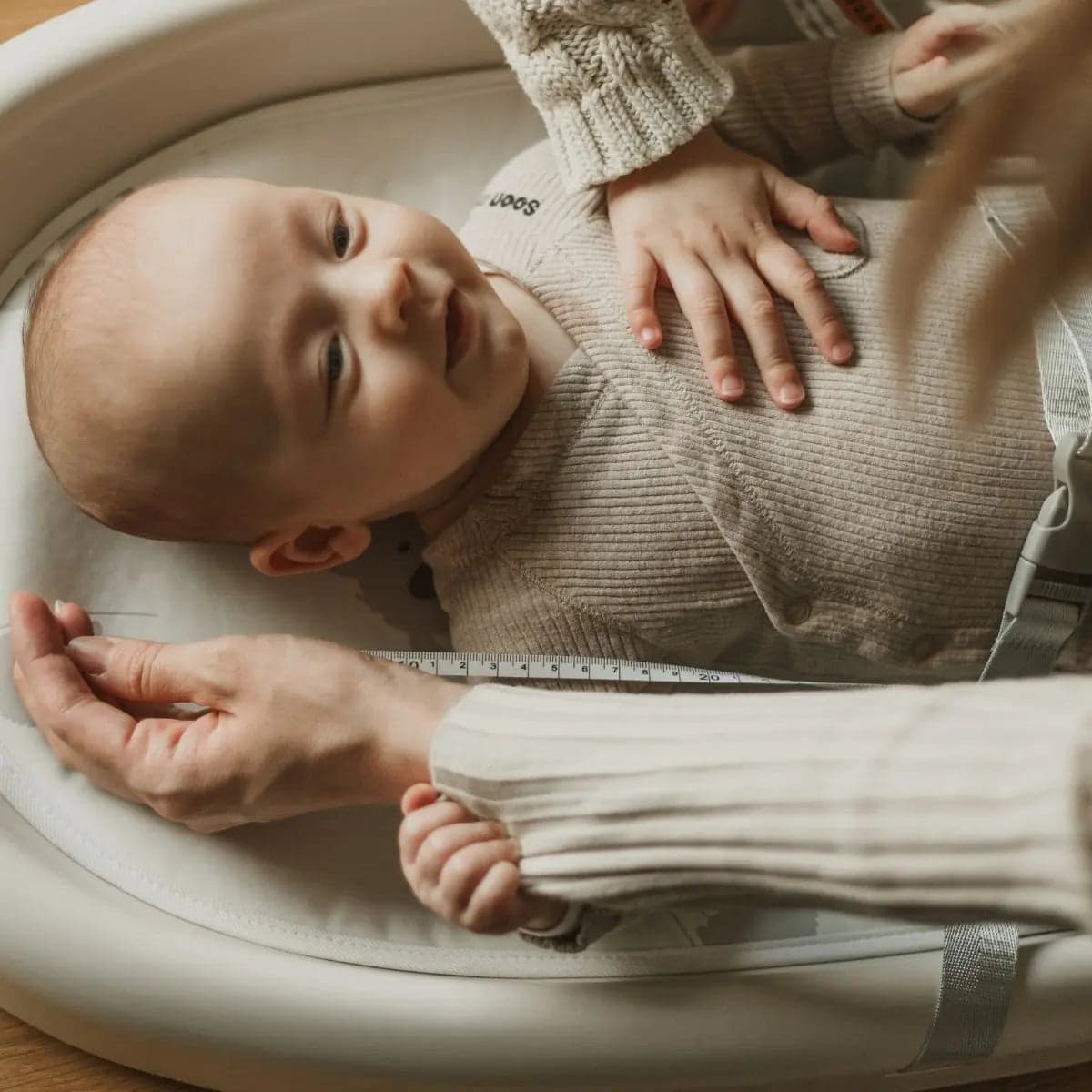 Baby lying on the contoured Cuddobaby changing pad while a caregiver uses the integrated length tape